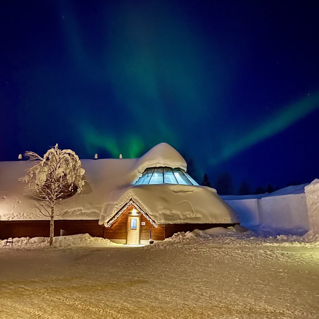 Casetta innevata sotto l'aurora boreale in Lapponia Finlandese